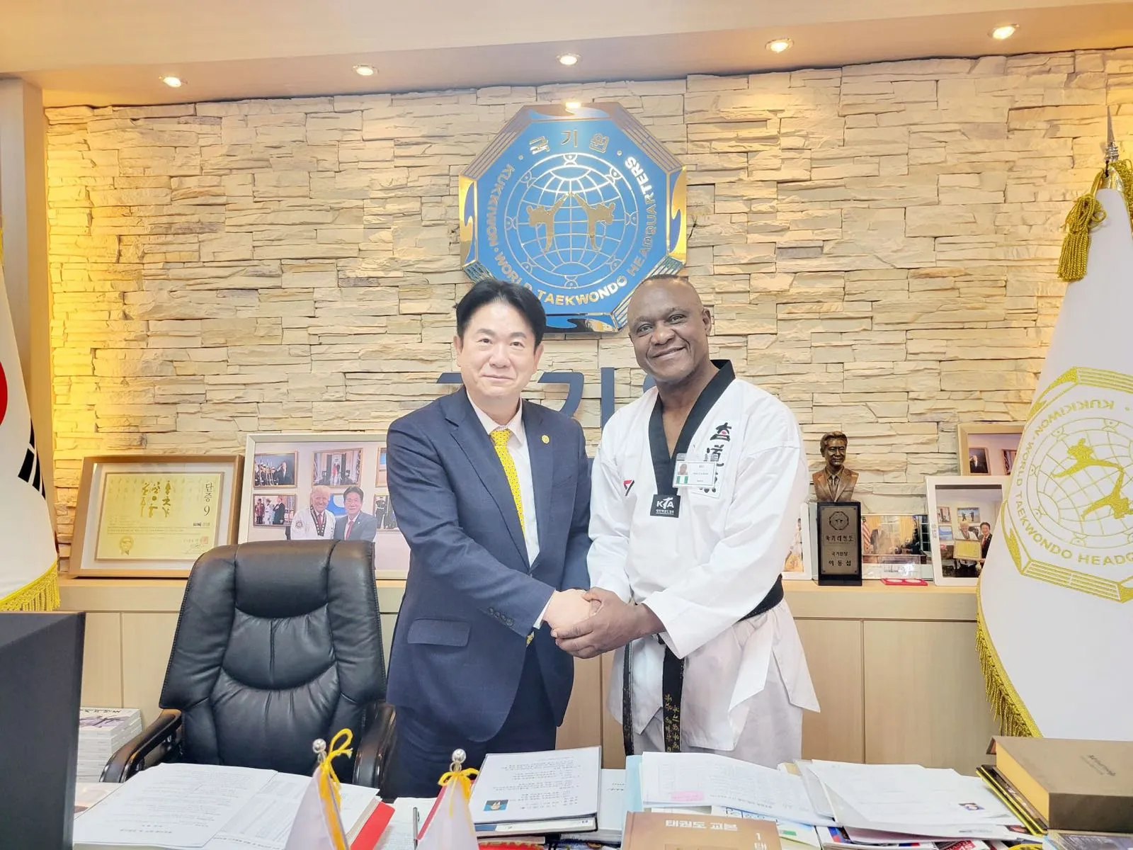 GrandMaster Pius Ilukhor shaking hands with the President of the Kukkiwon beneath the World Taekwondo Headquarters seal in Seoul, Korea