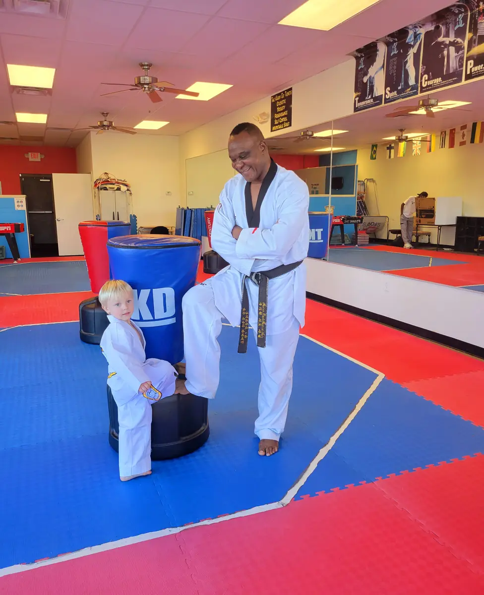 GrandMaster Pius with a young child in a Taekwondo uniform at Master Pius Martial Arts in Sandy Springs