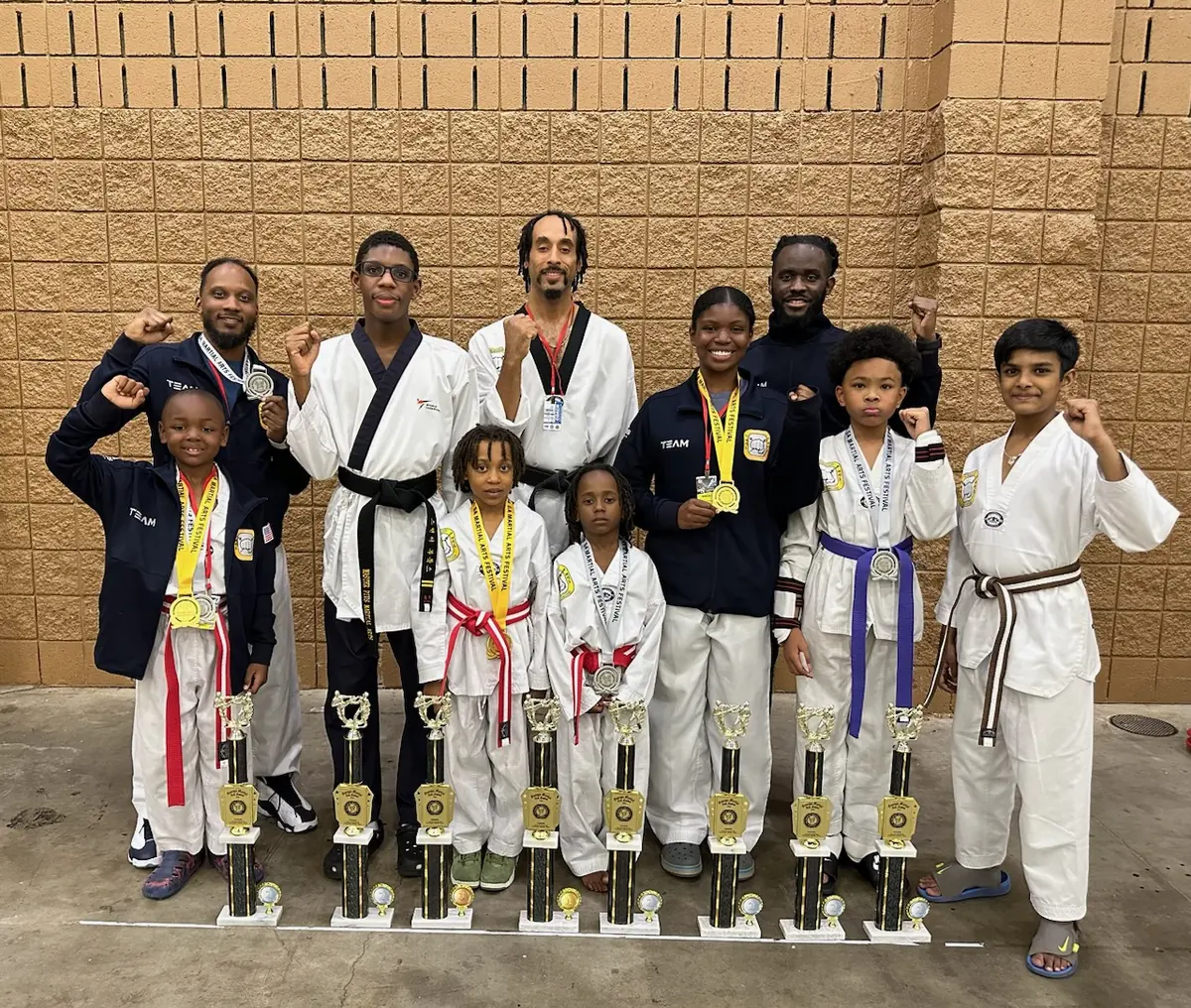 Master Pius Martial Arts students and instructors holding a row of tournament trophies, fists raised